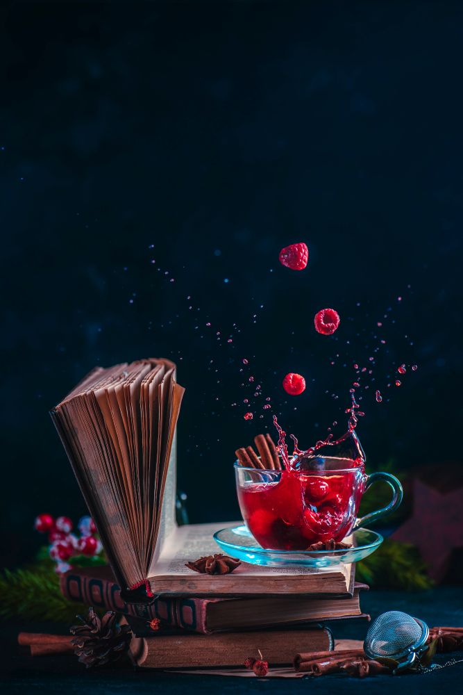 Red berry tea on a stack of books with a dynamic splash. Winter hot drink on a dark background with copy space
